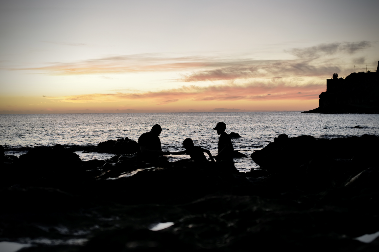 Maisemakuva Kanarialta. Auringonlasku jossa mies ja kaksi lasta valoa vasten.