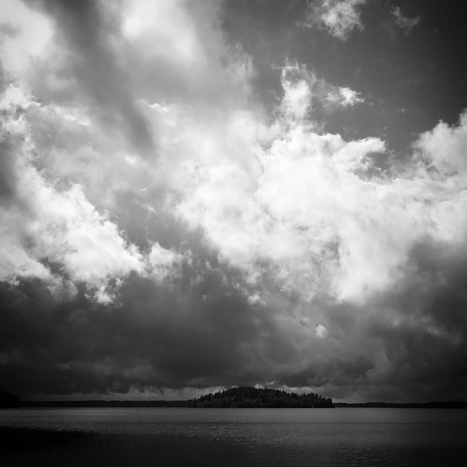 Mustavalkoinen kuva pilvistä ja järvenselästä. 